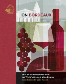 Red wine bottle, glass of red wine and grapes in front of vineyard and white building, on cover of 'On Bordeaux, Tales of the Unexpected from the World's Greatest Wine Region', by Academie du Vin Library.