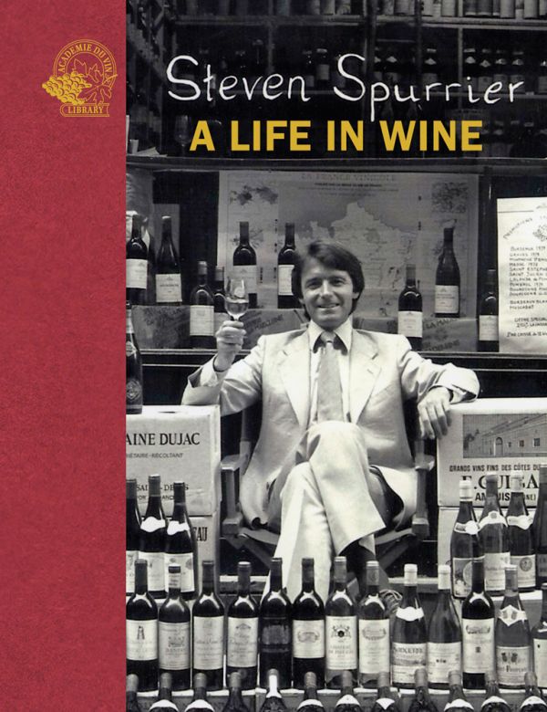 Book cover of Steven Spurrier, A Life in Wine, with the British wine expert and merchant sitting in chair, holding glass of wine, surrounded by stacks of wine. Published by Academie du Vin Library.