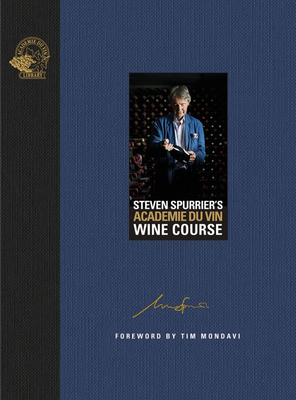 Man wearing blue jacket, standing in wine cellar, holding a bottle wine, on blue cover of 'Steven Spurrier's Académie du Vin Wine Course, The Art of Learning by Tasting', by Academie du Vin Library.