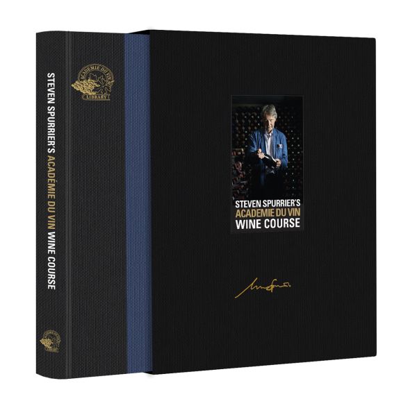 Man wearing blue jacket, standing in wine cellar, holding a bottle wine, on blue cover of 'Steven Spurrier's Académie du Vin Wine Course, The Art of Learning by Tasting', by Academie du Vin Library.