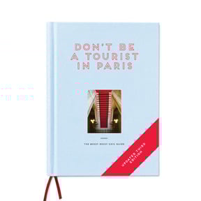 Book cover of Don't be a Tourist in Paris. with an aerial view of red stairs leading down to black and white checked tiled floor. Published by 13 Things Ltd.
