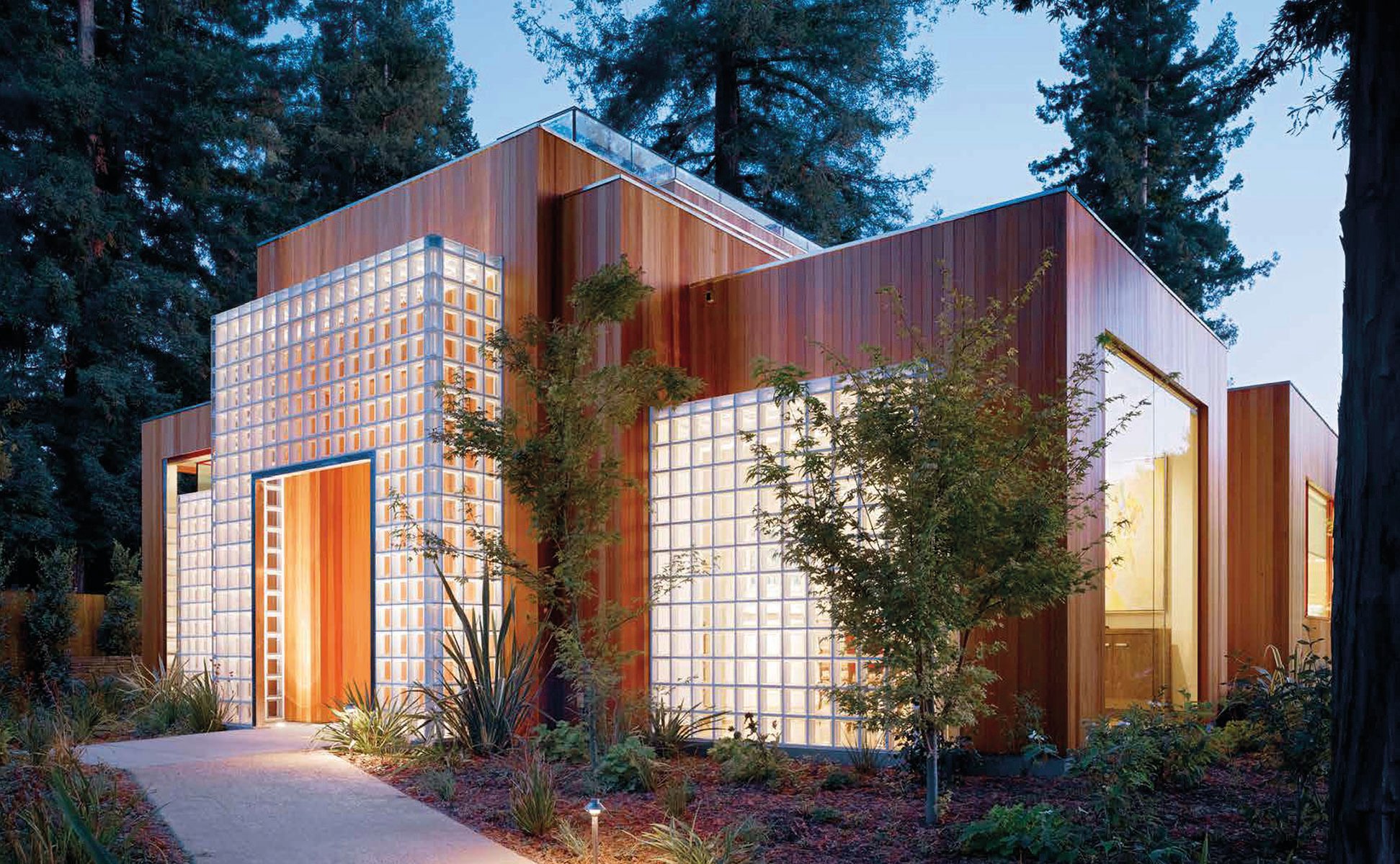 Façade of modern house with wood exterior and pale grey grid panels, surrounded by green trees, THE HOUSE OF LIGHT in white font to top right.