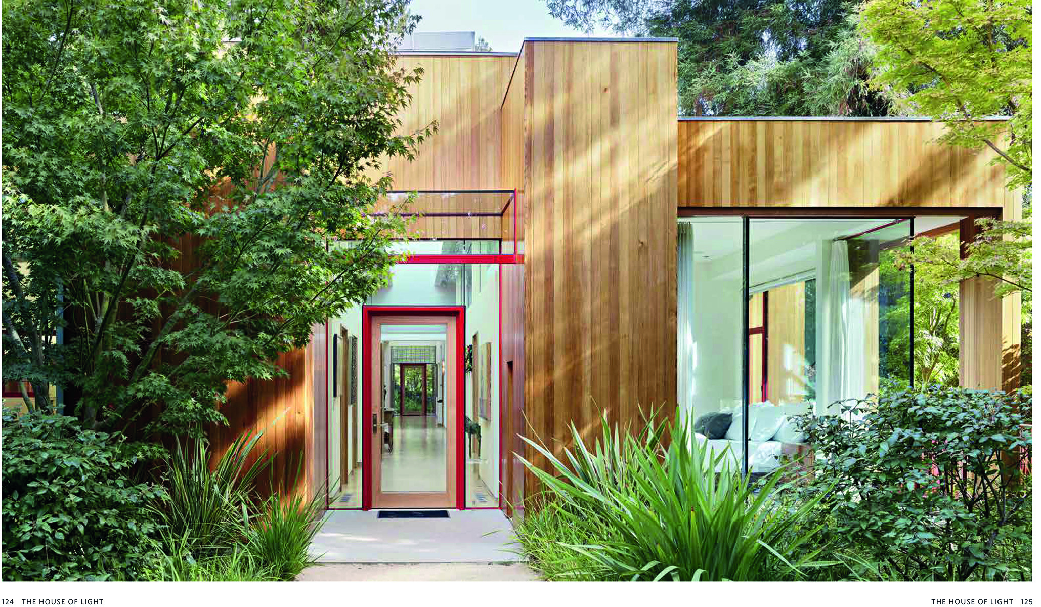 Façade of modern house with wood exterior and pale grey grid panels, surrounded by green trees, THE HOUSE OF LIGHT in white font to top right.