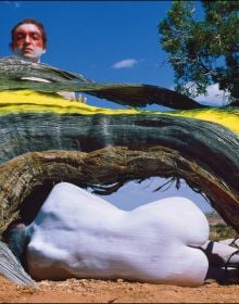 2 nude figure in red body paint and blue hair, 1 standing holding mannequin's legs, 1 sitting on edge of circular pool, blue cover, BODY MIRROR in white font above.