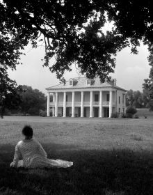 Blue cover with seated black model in white dress, holding scroll with Behind the Camera in white font above
