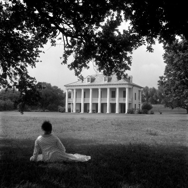 Blue cover with seated black model in white dress, holding scroll with Behind the Camera in white font above