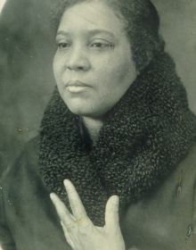 Blue cover with seated black model in white dress, holding scroll with Behind the Camera in white font above