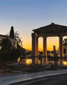Book cover of Athens Unveiled, with a pot of red flowers sitting on balustrade, with Greek female stone head sculpture, and mural. Published by ORO Editions.