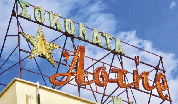 Book cover of Athens Unveiled, with a pot of red flowers sitting on balustrade, with Greek female stone head sculpture, and mural. Published by ORO Editions.