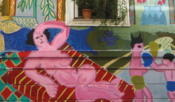 Book cover of Athens Unveiled, with a pot of red flowers sitting on balustrade, with Greek female stone head sculpture, and mural. Published by ORO Editions.