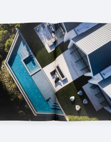 Modern, flat-roofed building with infinity pool and lounge chairs overlooking a green landscape. Published by ORO Editions.