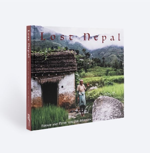 Book cover of Lost Nepal: A Photographic Memoir; featuring a figure standing in front of a hut with thatched roof, and misty mountains behind. Published by ORO Editions.
