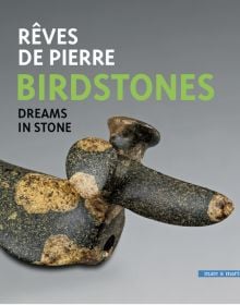 Dark stone bird like sculpture on grey background with Rêves de pierre Birdstones Dreams in stone in white green and black font above
