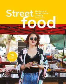 Chef Simona El-Harar holding a tub of food, food stall behind, on cover of 'Street food The Heart of Mediterranean Cooking', by Lannoo Publishers.