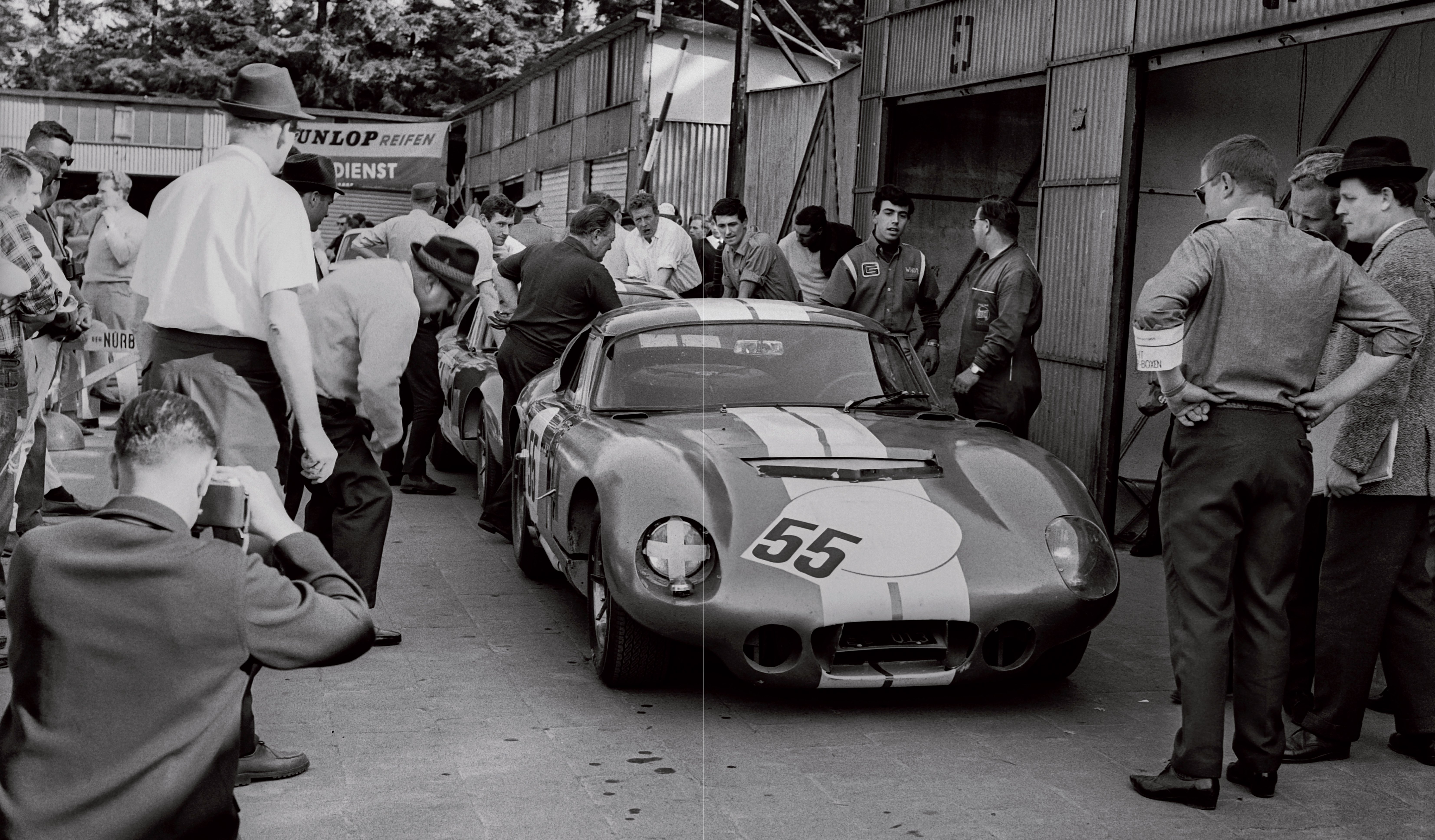 Black and white action photograph of a sports car on a sloped track with spectators on the side of the road with Johnny Rives Manou Zurini Editions Cercle D'Art Car Racing 1965 in white and beige