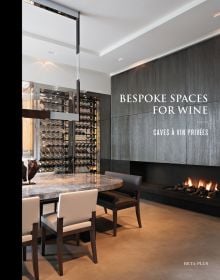 Minimalist interior, marble table, tall wine rack unit, lit fireplace, on cover of 'Bespoke Spaces for Wine', by Beta-Plus.