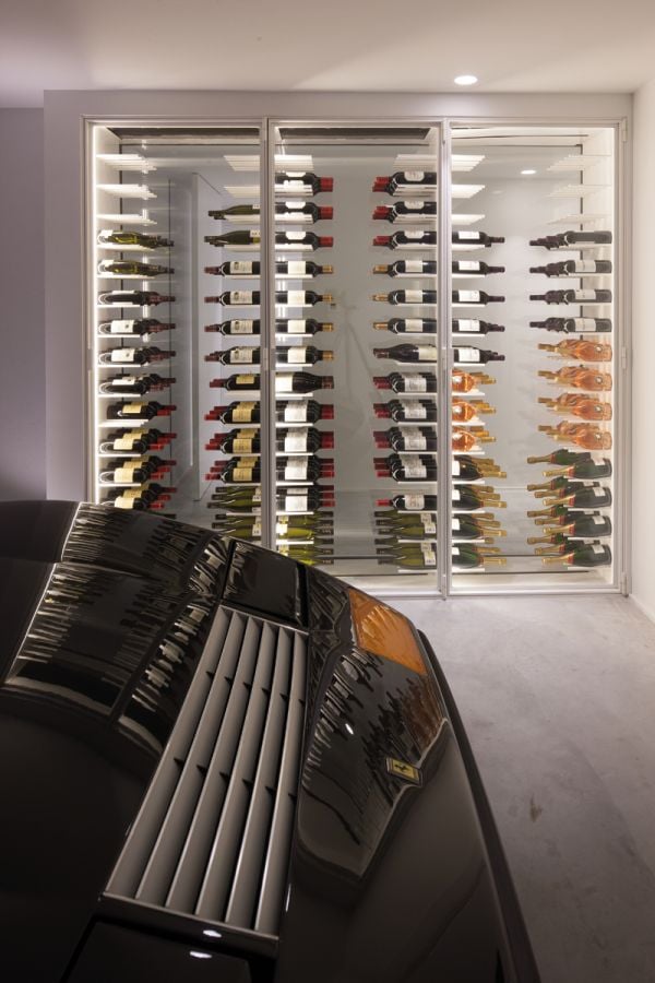 Minimalist interior, marble table, tall wine rack unit, lit fireplace, on cover of 'Bespoke Spaces for Wine', by Beta-Plus.