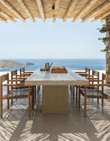 Chair and barrel table with drink on top, swimming pool, sea view behind, tall trees either side, on cover of 'Living by the Sea', by Beta-Plus.