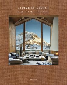 Book cover of Alpine Elegance: High-End Mountain Homes, featuring a cozy house with a view of snow topped mountains through the large windows. Published by Beta-Plus.