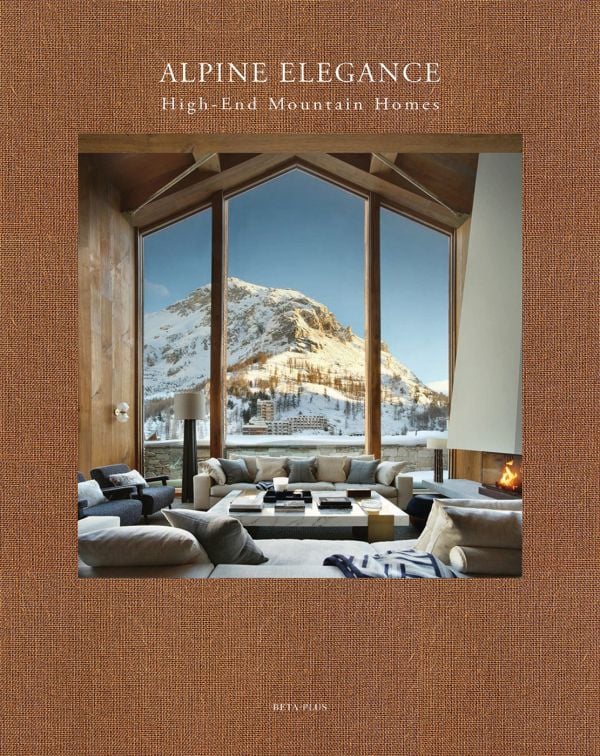 Book cover of Alpine Elegance: High-End Mountain Homes, featuring a cozy house with a view of snow topped mountains through the large windows. Published by Beta-Plus.