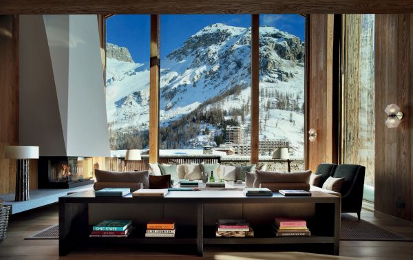 Book cover of Alpine Elegance: High-End Mountain Homes, featuring a cozy house with a view of snow topped mountains through the large windows. Published by Beta-Plus.