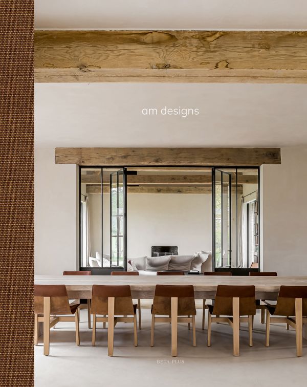 Book cover of am designs; featuring an interior living room with wood ceiling beams above a long table with chairs. Published by Beta-Plus.