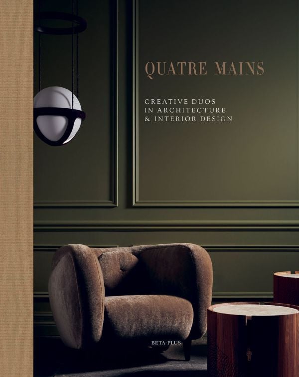 Book cover of Quatre Mains: Creative Duos In Architecture & Interior Design; featuring an interior room with dark green panelled walls and a large brown armchair. Published by Beta-Plus.