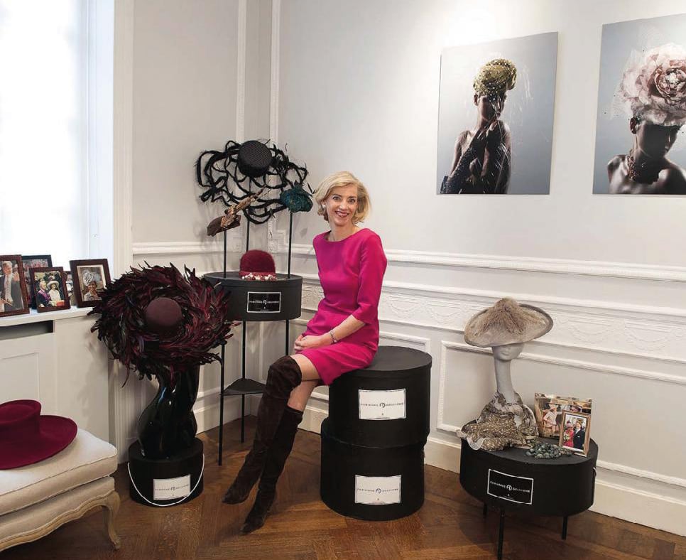 Fashion model in brown, blue and green feathered hat with black silk bow to centre, FABIENNE DELVIGNE in white font to lower right.