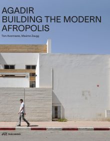 Man walking past white buildings in Moroccan city of Agadir, under blue sky, AGADIR BUILDING THE MODERN AFROPOLIS in black font above.