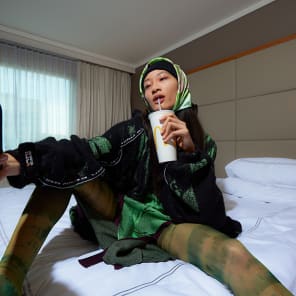 Head and shoulder green filtered shot of model, closed eyes in dress and long earrings, Wild Thing in white font below.