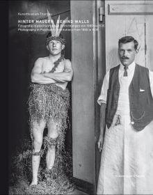 Book cover of Behind Walls: Photography in Psychiatric Institutions from 1880 to 1935, with a man in long white smock with waistcoat, and man in tribal dress, standing in doorway. Published by Scheidegger & Spiess.