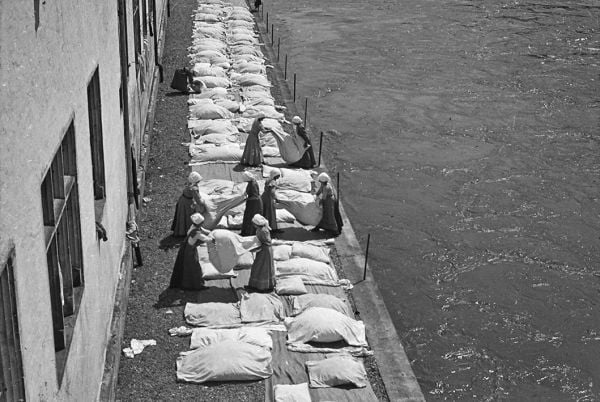 Book cover of Behind Walls: Photography in Psychiatric Institutions from 1880 to 1935, with a man in long white smock with waistcoat, and man in tribal dress, standing in doorway. Published by Scheidegger & Spiess.
