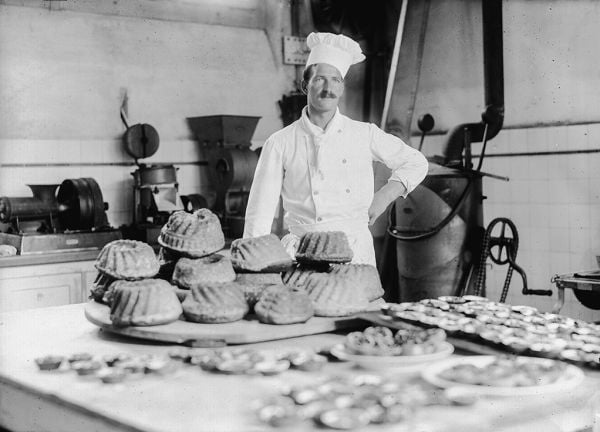 Book cover of Behind Walls: Photography in Psychiatric Institutions from 1880 to 1935, with a man in long white smock with waistcoat, and man in tribal dress, standing in doorway. Published by Scheidegger & Spiess.