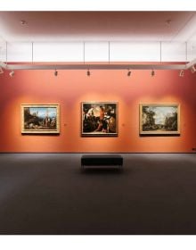 Two low black seats on pine flooring with shafts of light bursting through museum window slats with The Collection in a New Light Kunsthaus Zürich in bright yellow font