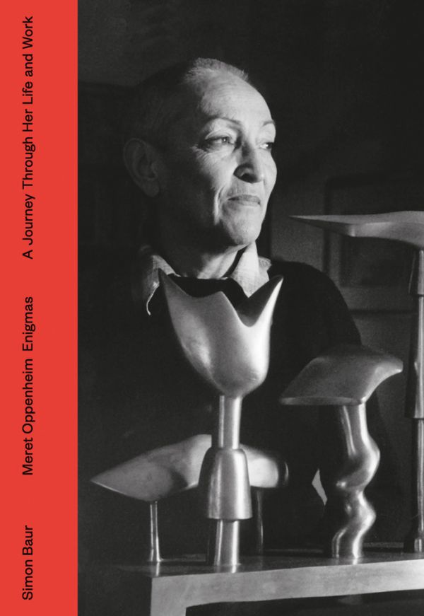 Book cover of Simon Baur Meret Oppenheim Enigmas A Journey Through Life and Work, with the artist and photographer smiling, in front of sculpture. Published Scheidegger & Spiess.