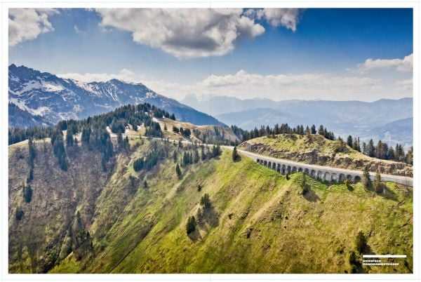 Aerial view of mountainous green landscape with winding roads, surrounded by lakes, on cover of 'Curves: Germany, Band 13: Baden-Württemberg / Bayern' by Delius Klasing Verlag GmbH.