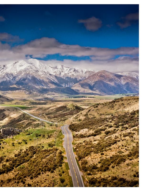 Book cover of Stefan Bogner's CURVES New Zealand: Volume 22, with a winding road on the coast, with snow covered mountains behind. Published by Delius Klasing.