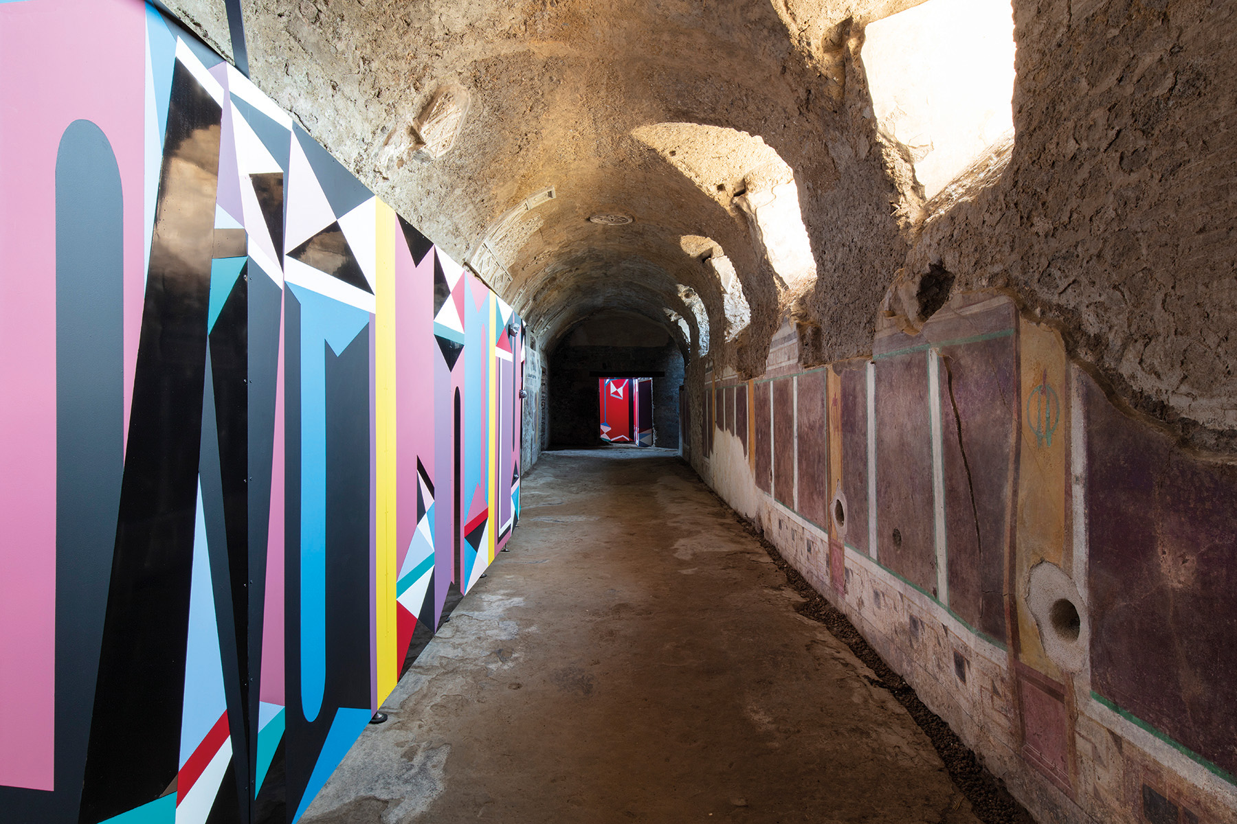 Installation wall with red, black, white, blue triangle shape patterns, Catrin Huber in white font to centre left