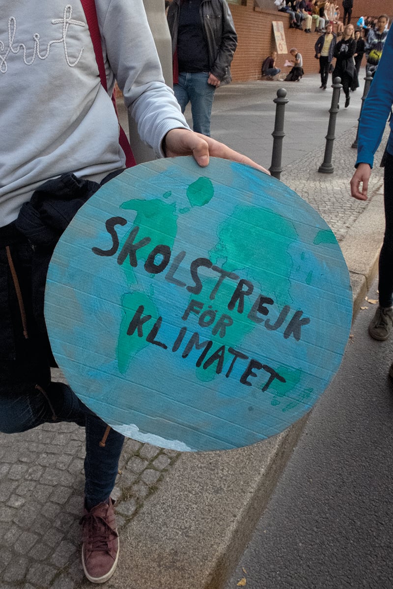 View of back of climate change protestors holding placards for Fridays for Future, WIR SIND HIER SIND LAUT FRIDAYS FOR FUTURE in red font across cover.