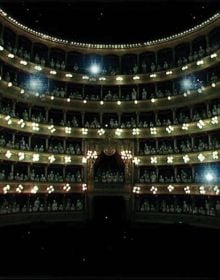 String lights with illuminated light bulbs hanging down in exhibition space, Opera Opera Allegro ma non troppo in red font to centre, by Kerber.