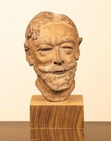 Sculpture of male head with large moustache, mounted on wood plinth.