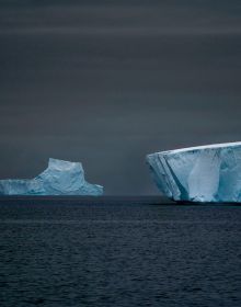 Two large icebergs floating on water in Antarctica, TOM NAGY, SOLITAIRE, in white font above.