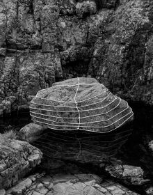 Large grey rock bound in rope, on coastal edge, on cover of 'Anna Reivilä, Nomad', by Kerber.