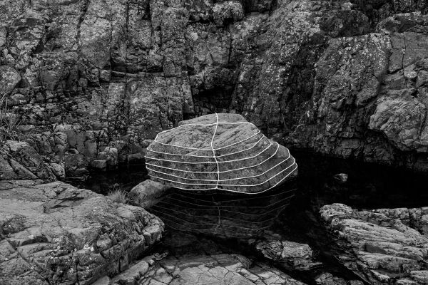 Book cover of Anna Reivilä, Nomad, with a large grey rock bound in rope, on coastal edge. Published by Kerber.