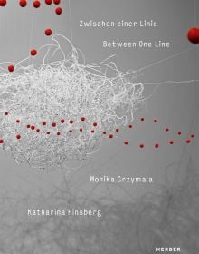 Book cover of Between One Line: Katharina Hinsberg & Monika Gryzmala, with an art installation of white wire and small red balls. Published by Kerber.