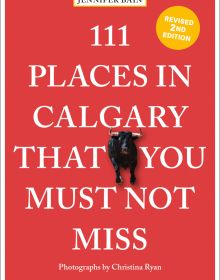 Black bull near centre of red cover of '111 Places in Calgary That You Must Not Miss', by Emons Verlag.