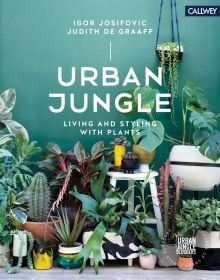 Potted indoor plants, cacti and succulents, against green wall, URBAN JUNGLE LIVING AND STYLING WITH PLANTS in white font above.