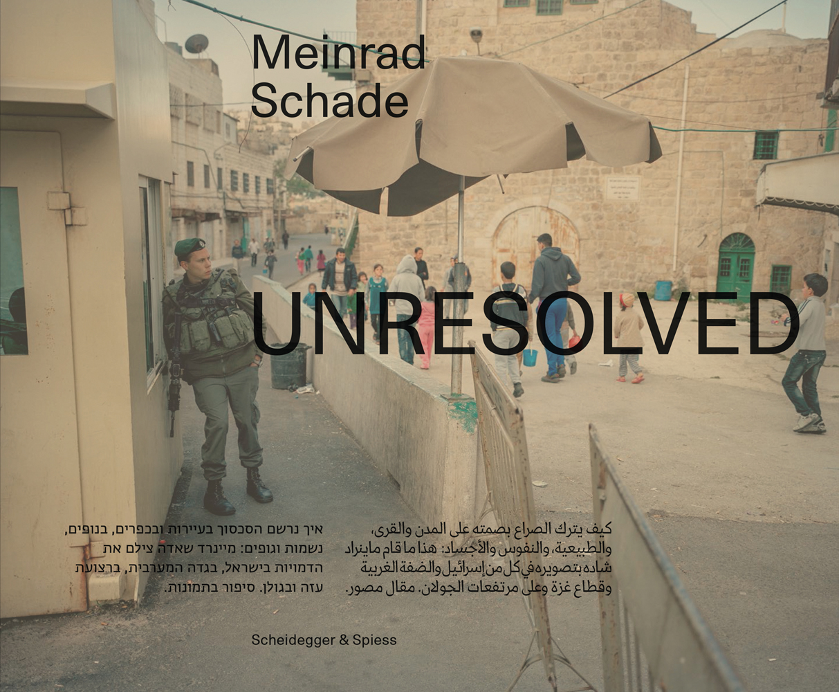 Book cover of Unresolved; with a camouflaged soldier leaning on building, with townspeople walk past brick building. Published by Scheidegger & Spiess.