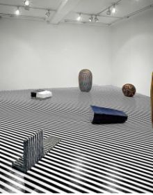 Ceramic glazed sculpture of head on low table, orange cover, Jun Kaneko The Space Between in white font to upper left.