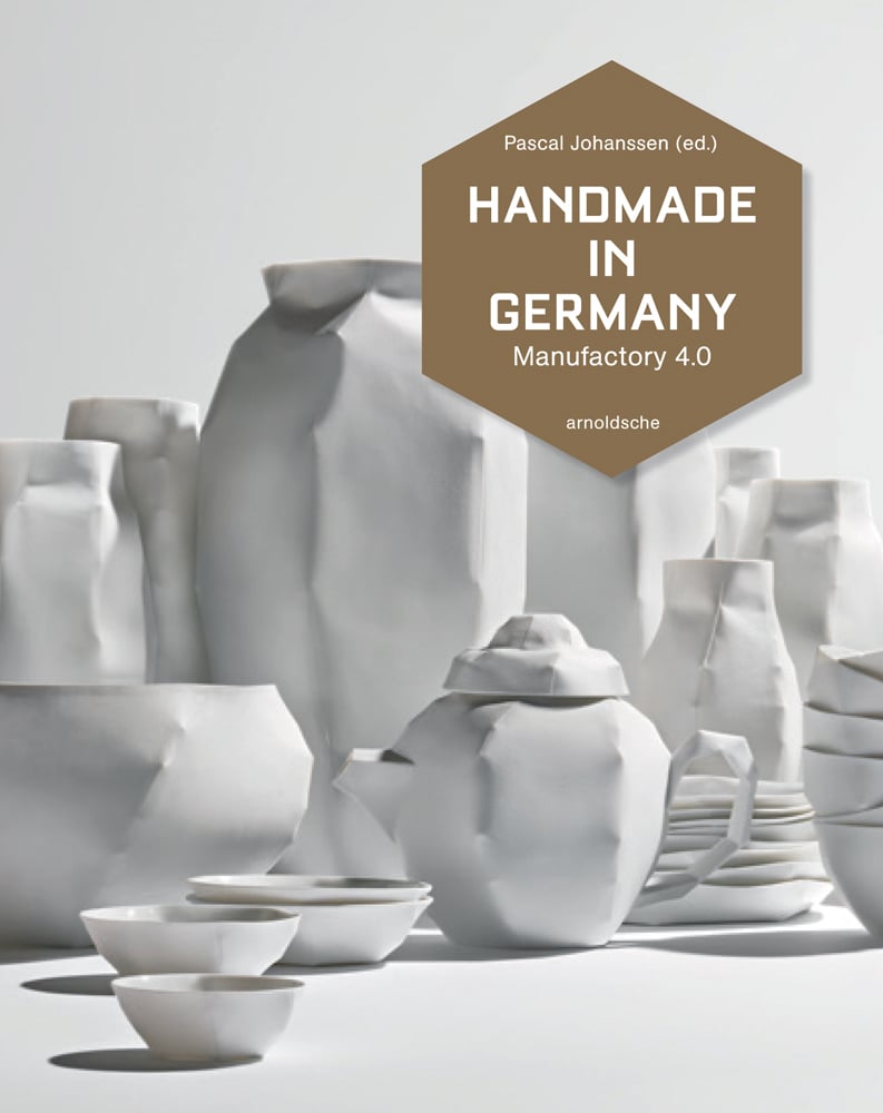 Still life collection of white ceramic tableware in folded paper style, white cover, HANDMADE IN GERMANY in white font on hexagonal brown shape.